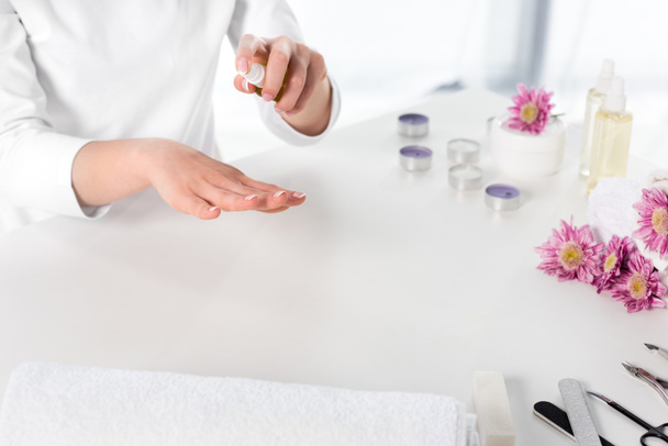 vista parcial de la mujer usando aceite de aroma en la mesa con toallas, flores, velas e instrumentos para la manicura en el salón de belleza
 - Foto, Imagen