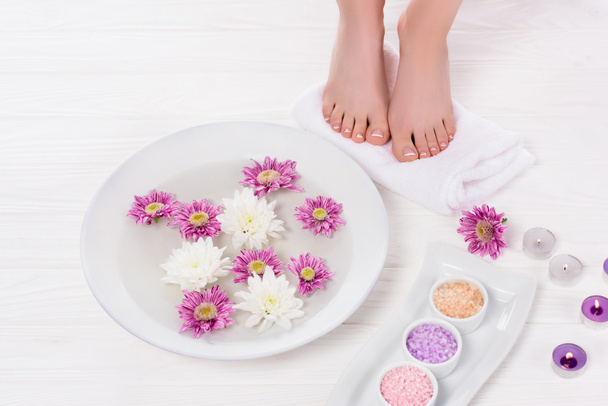 partial view of barefoot woman receiving bath for nails with colorful sea salt and flowers near aroma candles in beauty salon - Foto, Imagem