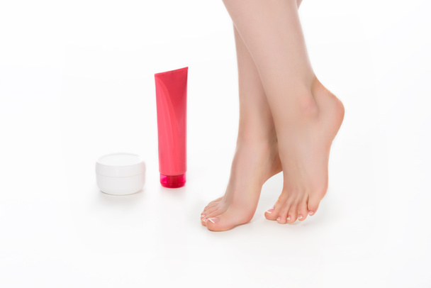 gedeeltelijke weergave van barefoot vrouw met crème containers voor skin care geïsoleerd op witte achtergrond  - Foto, afbeelding