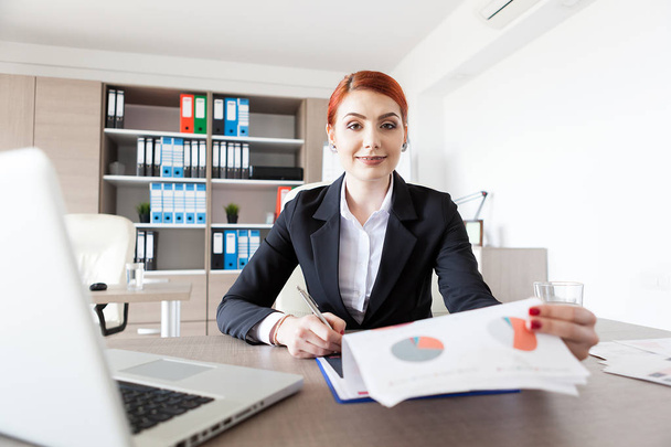 Redhead young businesswoman in her office checking documents - Foto, imagen
