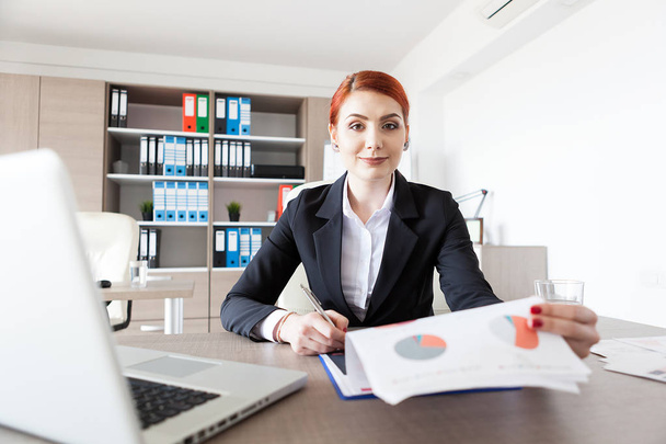 Redhead young businesswoman in her office checking documents - Photo, Image