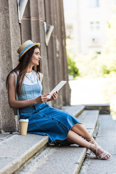 young smiling woman with tablet and coffee to go resting on steps on street - Foto, Imagem