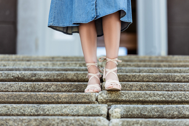 cropped shot of woman in denim skirt and fashionable shoes walking down steps - Фото, изображение