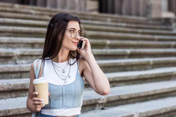Portret młodej kobiety z kawą do przejdź rozmawiać na smartphone na ulicy - Zdjęcie, obraz