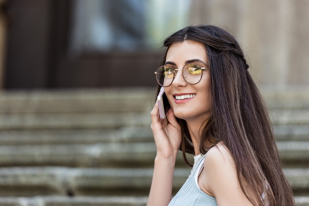 junge lächelnde Frau mit Brille, die auf der Straße mit dem Smartphone spricht - Foto, Bild