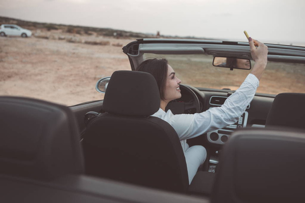 Happy girl photographing herself on smartphone in car  - Φωτογραφία, εικόνα