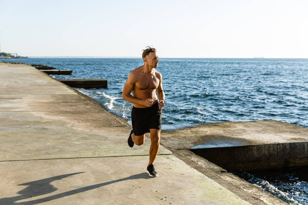 красивый взрослый мужчина без рубашки бегает по берегу моря
 - Фото, изображение