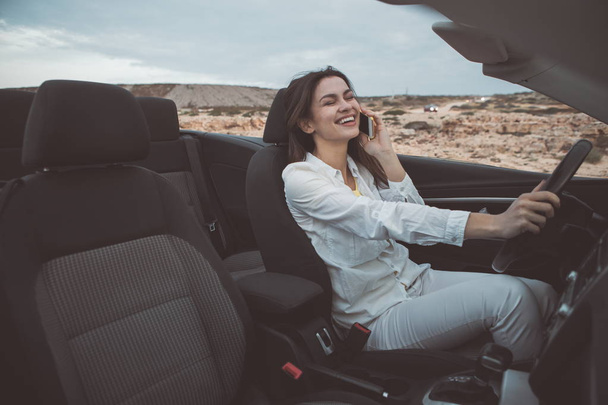 Χαρούμενη κοπέλα μιλώντας στο smartphone σε μετατρέψιμο αυτοκίνητο  - Φωτογραφία, εικόνα