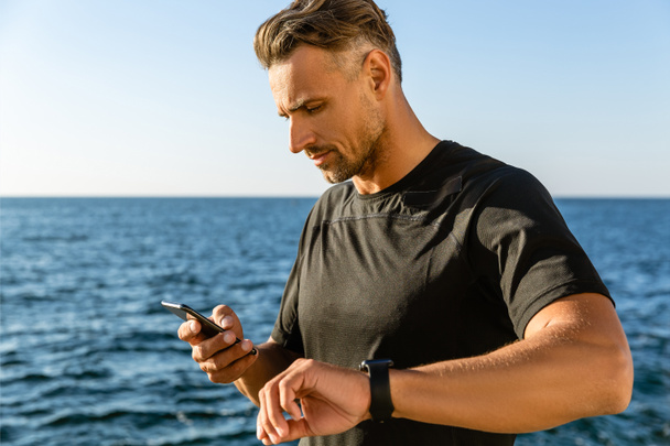 bel homme adulte utilisant smartphone et montre intelligente sur le bord de la mer
 - Photo, image