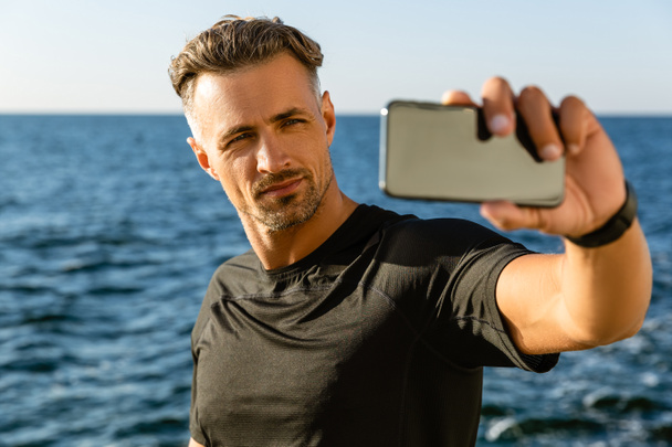 knappe volwassen man nemen selfie met smartphone aan kust - Foto, afbeelding