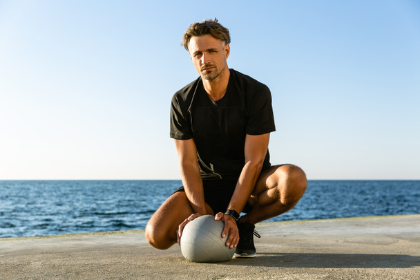 szép felnőtt ember ül a fit ball, a tengerparton, és látszó-on fényképezőgép - Fotó, kép