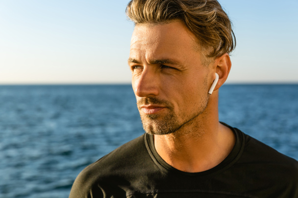 portrait en gros plan d'un bel homme adulte avec écouteurs sans fil sur le bord de la mer regardant loin
 - Photo, image