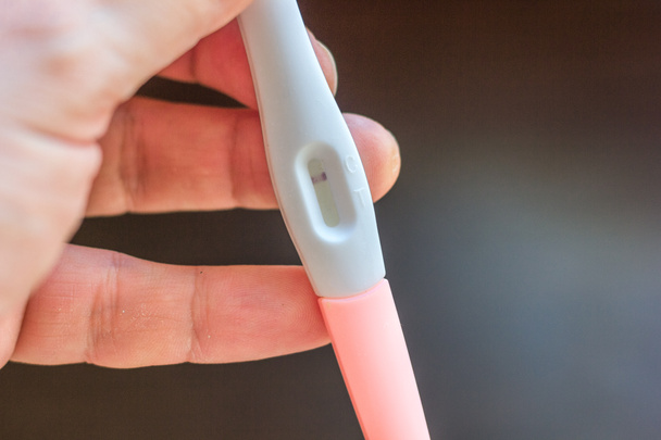 Το χέρι κρατά αρνητικό τεστ εγκυμοσύνης πάνω από το καφέ φόντο - Φωτογραφία, εικόνα