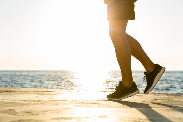 colpo ritagliato di atleta che fa jogging sulla riva del mare davanti all'alba
 - Foto, immagini