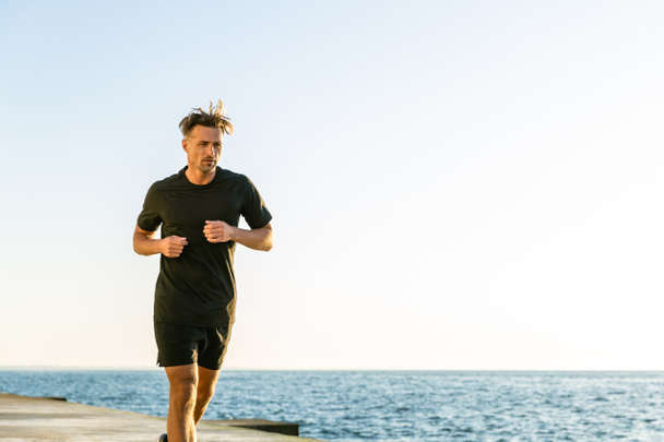athletic adult joger running on seashore in morning - Photo, Image