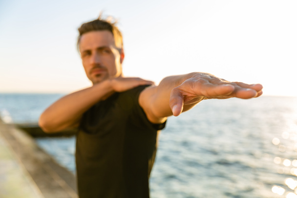 крупным планом взрослый спортсмен растягивает руку перед тренировкой на берегу моря
 - Фото, изображение
