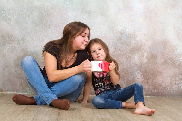 Cute little girl and her beautiful young mother sitting together on the floor. - Photo, Image