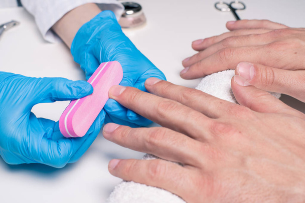 Manicure dla mężczyzn. Kosmetyczki w gumowe rękawice plik paznokcie na męskie dłonie. - Zdjęcie, obraz