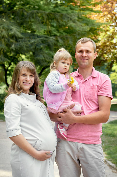 Mujer embarazada con marido hombre y niña linda pequeña hija en la naturaleza del parque. Concepto de familia feliz
  - Foto, imagen