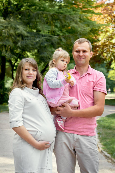 Pregnant woman with husband man and small cute daughter girl in park nature. Happy family concept  - Photo, Image