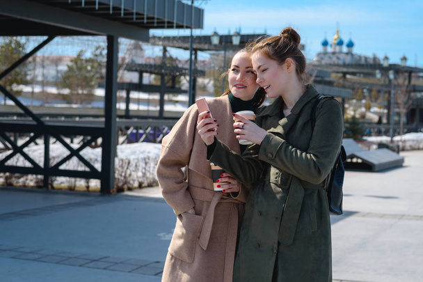 Dos jóvenes estudiantes viajeros en un abrigo al caminar por las calles de Kazán, utilizar un teléfono inteligente con un navegador
 - Foto, imagen