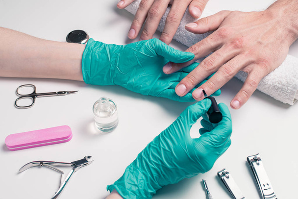 Manicure dla mężczyzn. Kosmetyczka w gumowych rękawiczkach, zastosować ochronny lakier do paznokci - Zdjęcie, obraz