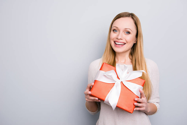 Portrait with copyspace empty place of cheerful positive girl having gift box in red package with white bow isolated on grey background looking at camera - Photo, Image