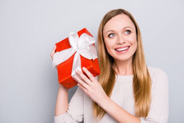 Portrait of excited successful girl want to know what inside of gift box in red package with white bow isolated on grey background having beaming smile - Photo, image