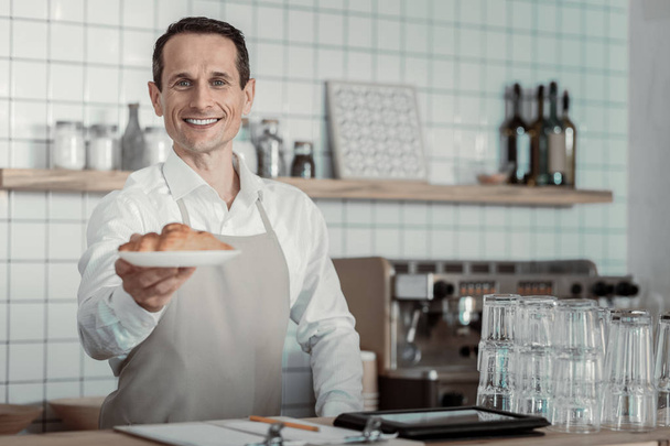 Fresh pastry. Delighted brunette expressing positivity while proposing tasty croissants - 写真・画像