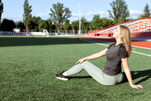 Young woman in sportswear sitting on the grass in the stadium. - 写真・画像