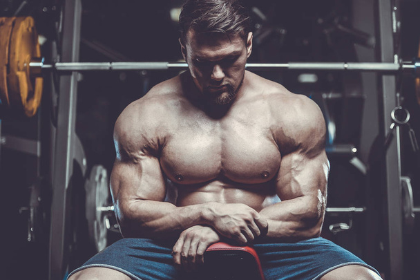 Handsome muscle caucasian man of model appearance bodybuilder workout in gym training chest pumping up pectoral muscles with dumbbells and on crossovers fitness bodybuilding and sport nutrition concept - Foto, Imagen