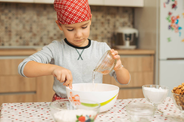 Menino derramando água em uma tigela enquanto mistura ingredientes para cozinhar
 - Foto, Imagem