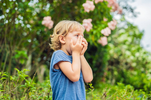 Little boy sneeze in the park against the background of a flowering tree. Allergy to pollen concept. - Photo, image