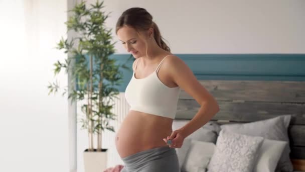 Veselá těhotná žena měření břiše v ložnici - Záběry, video