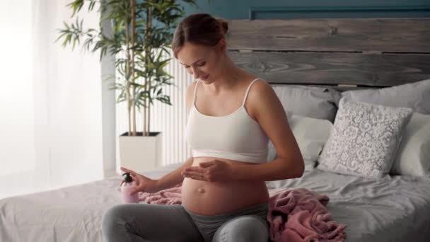 Νεαρή έγκυος γυναίκα, εφαρμογή ενυδατική κρέμα στην κοιλιά της - Πλάνα, βίντεο
