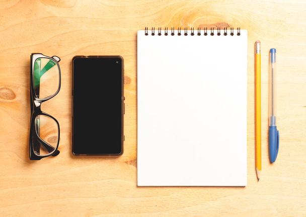 Business essentials. Top view of spiral blank notebook and smartphone on wood desk background - Photo, Image