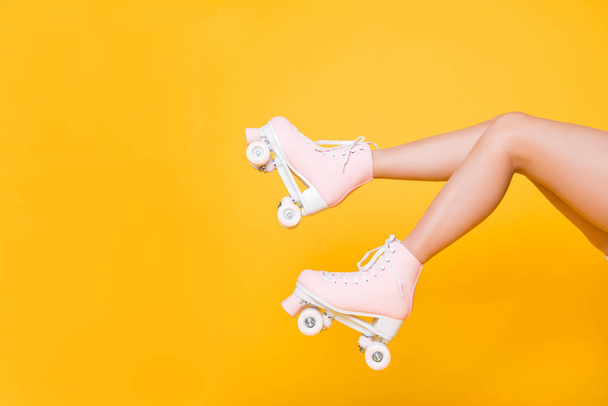 Cropped portrait of legs in pink vintage quad roller skates shoes isolated on yellow background, extreme balance concept, street outside urban lifestyle style, laser hair removal perfect skin - 写真・画像