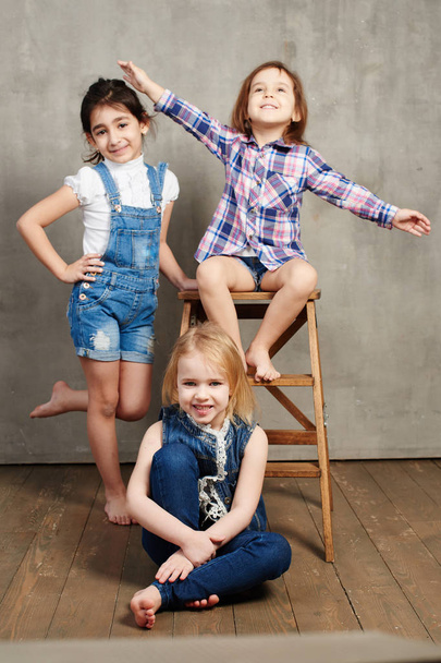 three girls with wooden chair posing on  concrete wall background  - Fotó, kép