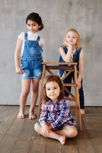 three girls with wooden chair posing on  concrete wall background  - Φωτογραφία, εικόνα