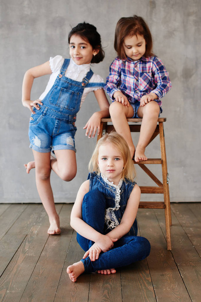 three girls with wooden chair posing on  concrete wall background  - Foto, Imagen