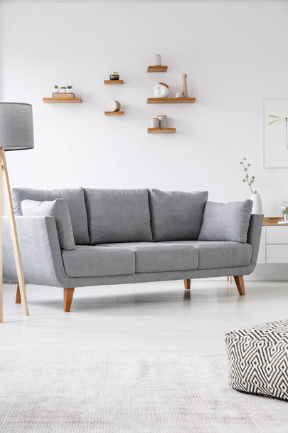 Grey couch in simple bright living room interior with pouf and lamp. Real photo - Фото, зображення