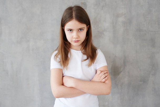 Portrait of little girl in white t-shirt with crossed arms posing on grey background  - 写真・画像