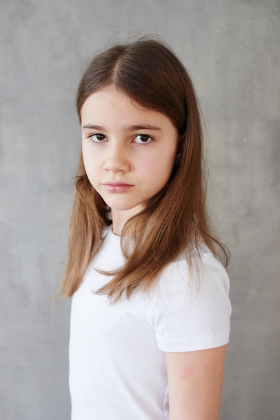 Portrait of little girl in white t-shirt posing on grey background  - Zdjęcie, obraz