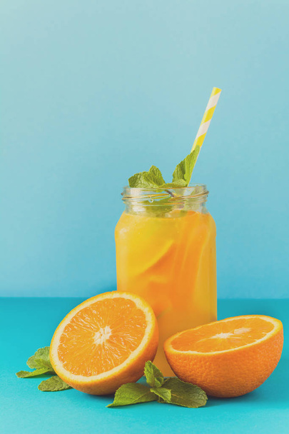 Jar with orange lemonade, decorated ice and mint on blue paper background. Toned - Foto, imagen