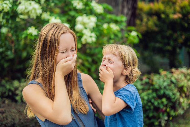 Mom and son sneeze in the park against the background of a flowering tree. Allergy to pollen concept. - Fotoğraf, Görsel