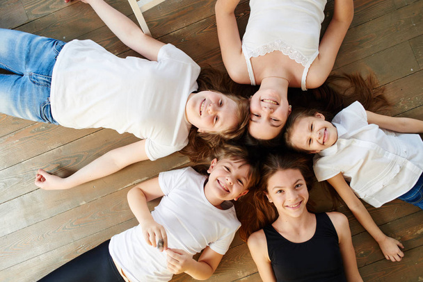 Five girls lying in shape of circle on wooden floor, top view - Foto, Imagem