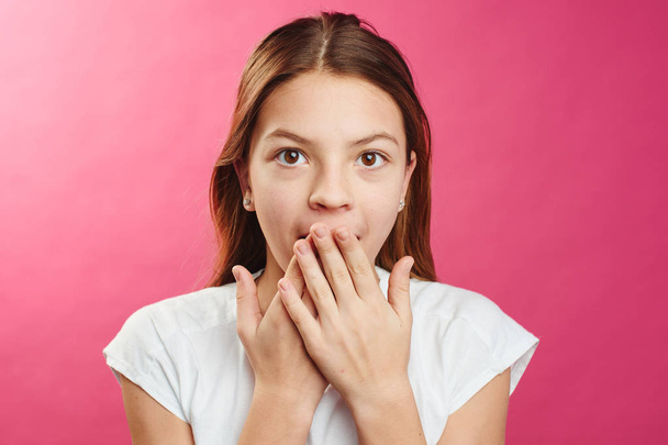 Portrait of surprised girl closed mouth with hands on pink background - Фото, изображение