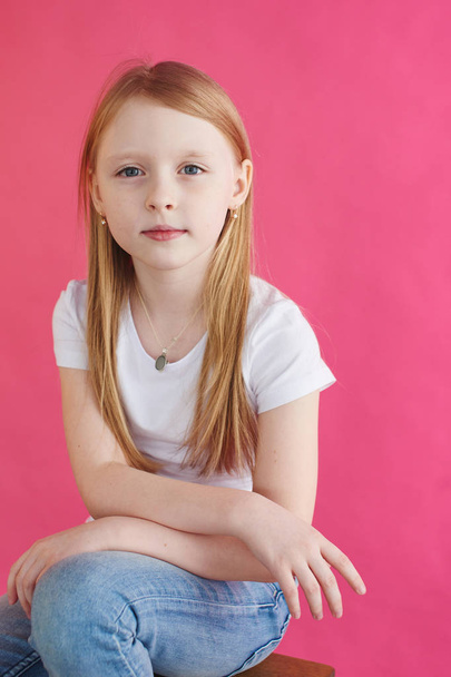 Little blonde girl sitting on wooden chair with pink wall on background - Φωτογραφία, εικόνα