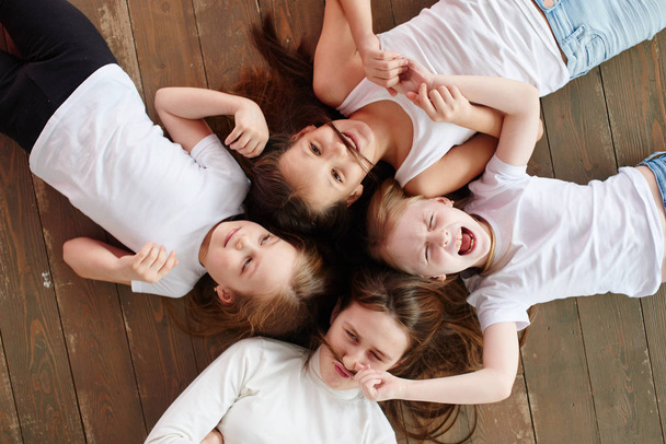 Four girls lying on wooden floor, top view  - Foto, immagini