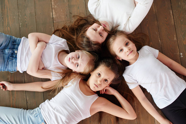 Four girls lying on wooden floor, top view  - 写真・画像